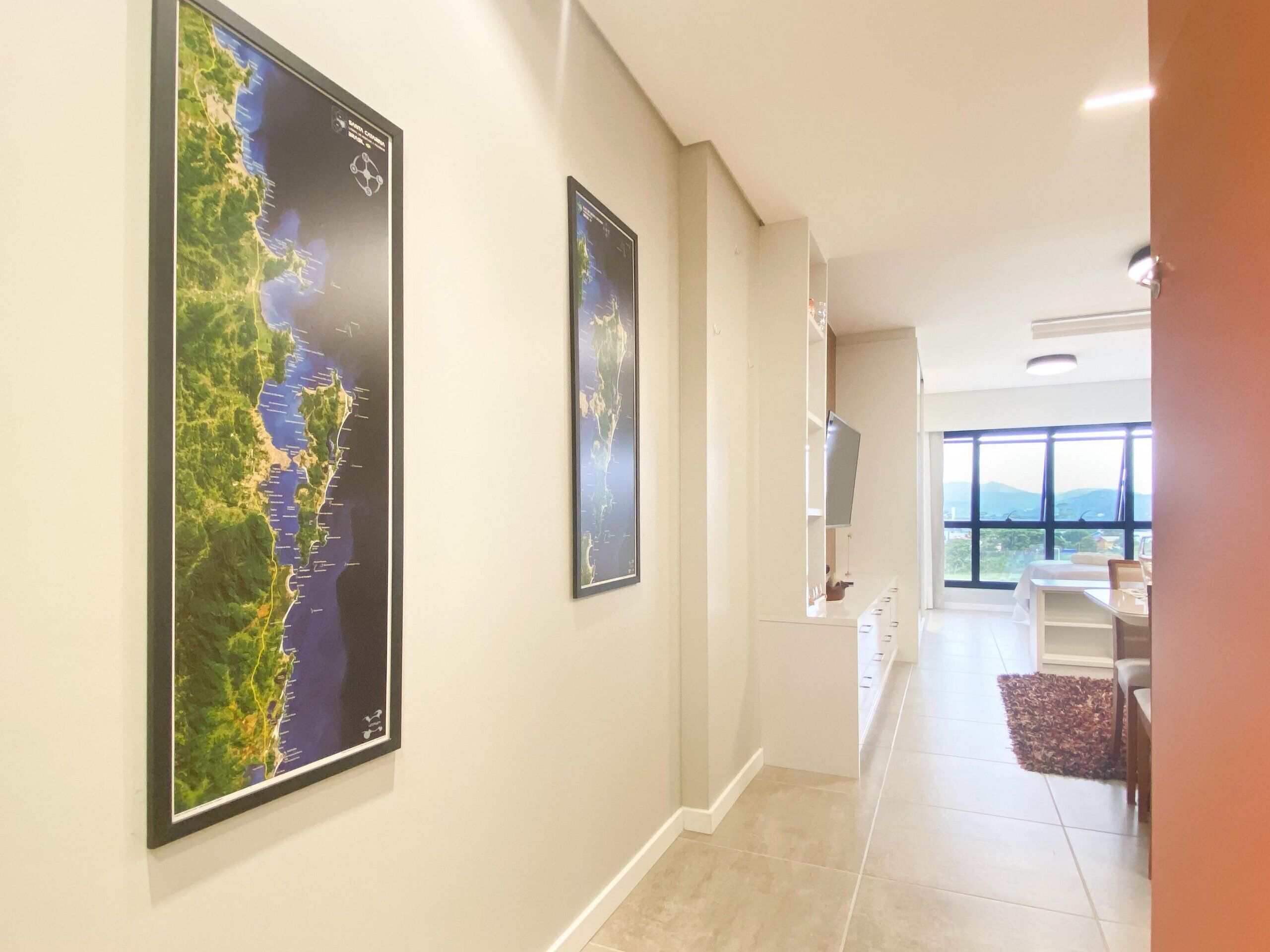 A hallway with two large framed maps on the wall, a dining area with a view, and a TV mounted on the wall.