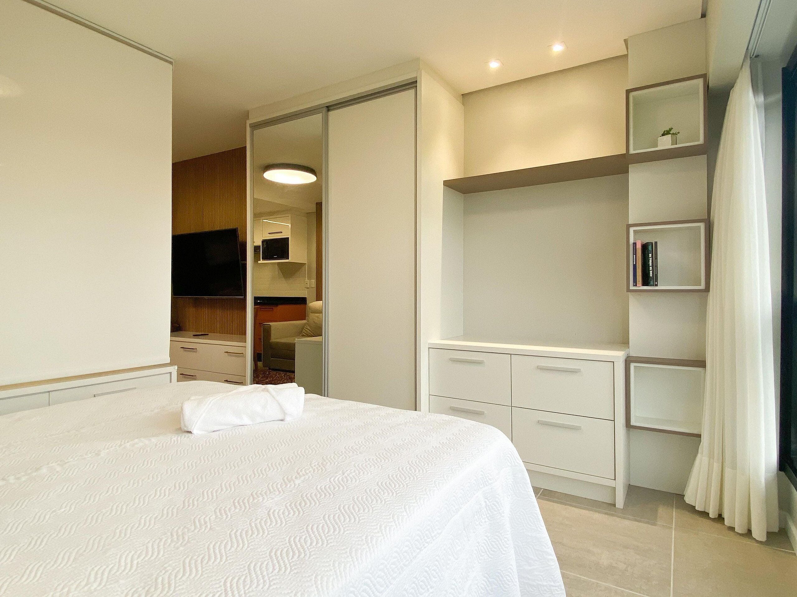 A hotel room with a large bed, a walk-in closet, a television, and a bookshelf.