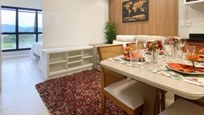 A modern dining area with a large window, a dining table set for four, and a view of the outdoors. - Studio Shopping OKA Floripa - SOK232 (Florianopolis)