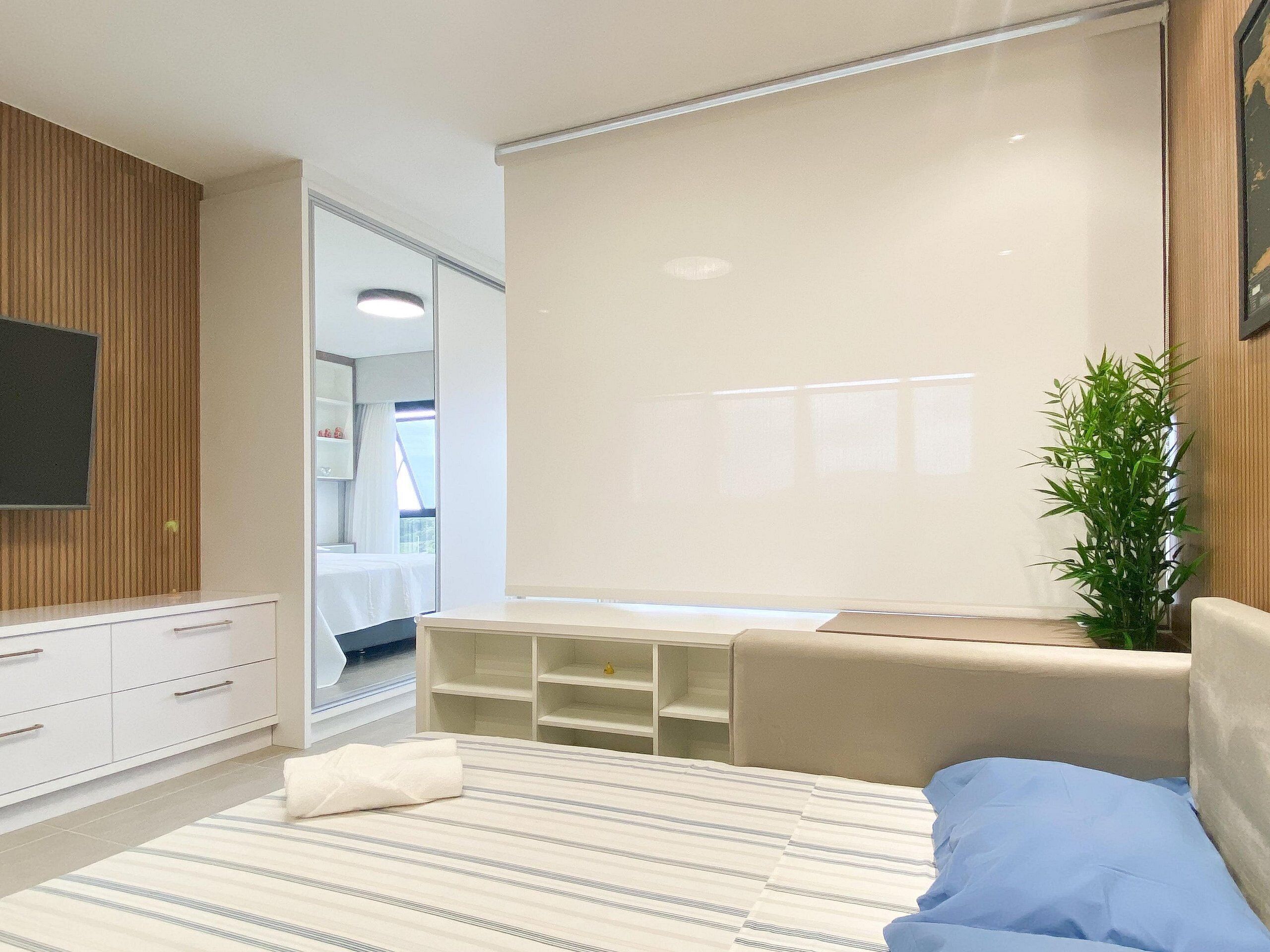 Een moderne slaapkamer met een bed, een televisie, een plant en een groot raam.