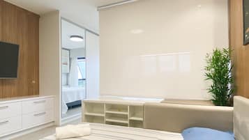 Een moderne slaapkamer met een bed, een televisie, een plant en een groot raam.