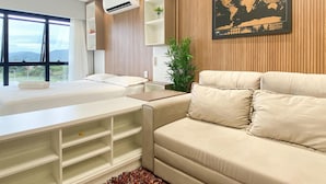 A modern hotel room with a bed, a sofa, a desk, and a large window offering a view of the outdoors.