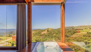 A room with a large window, a wooden deck, and a hot tub. - Cabana com vista e jacuzzi VST007 (Anitapolis)