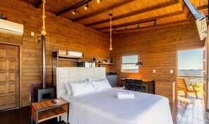 Ein Schlafzimmer in einer Holzhütte mit Bett, Nachttisch und Blick ins Freie.