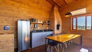 A compact kitchen with a refrigerator, microwave, and stove, a wooden dining table, and a large window offering a view of the landscape. - Cabana vista panorâmica e jacuzzi VST022 (Anitápolis)