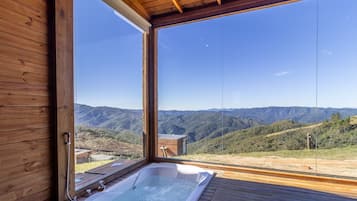 Una cabaña de madera con jacuzzi y vistas a un paisaje montañoso.