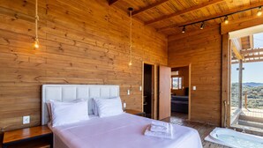 A wooden cabin bedroom with a bed, bedside table, and a view of the outdoors. - Cabana vista panorâmica e jacuzzi VST022 (Anitápolis)