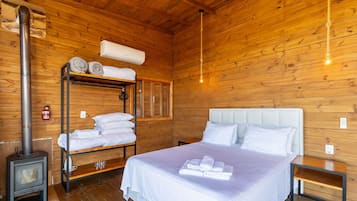 En stuga med träpanel, inredd med en våningssäng, en säng med vita sängkläder, en värmare och en väggmonterad luftkonditioneringsanläggning.