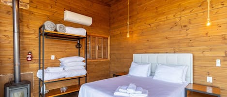 A wooden cabin room with a bunk bed, a bed with white linens, a heater, and a wall-mounted air conditioner.