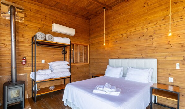 A wooden cabin room with a bunk bed, a bed with white linens, a heater, and a wall-mounted air conditioner.