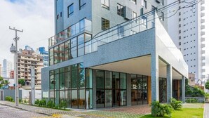 A modern building with a glass facade, a covered entrance, and a paved area with a drainage grate. - CJC Short Stay Ilusion (Natal)