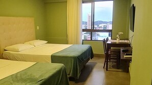 A hotel room with two beds, a dining table, and a view of a cityscape. - CJC Short Stay Ilusion (Natal)