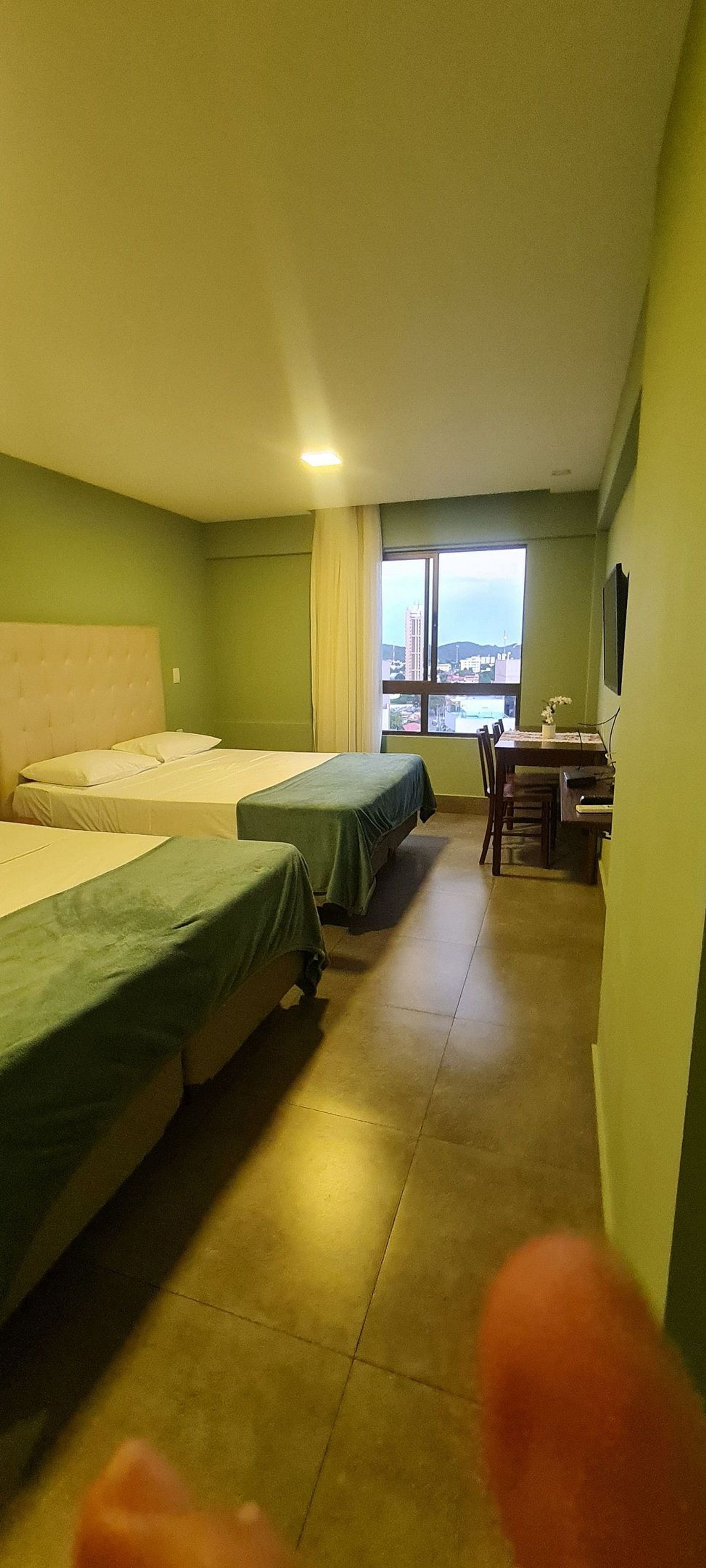 Quarto de hotel com duas camas, uma mesa de jantar e vista para a cidade.