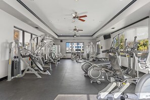 A gym with various exercise machines, ceiling fans, and large windows.