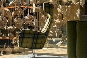 A modern chair with a unique design, a green sofa, and a wall with hanging leaf-like decorations. - Monverde - Wine Experience Hotel - by Unlock Hotels (Borba de Godim)