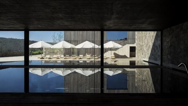 A modern interior with a large reflective pool, a stone wall, and a view of an outdoor area with umbrellas. - Monverde - Wine Experience Hotel - by Unlock Hotels (Borba de Godim)