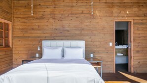 A wooden-paneled room with a bed, bedside tables, and a door leading to a bathroom. - Cabana vista Serra Catarinense VST023 (Anitápolis)