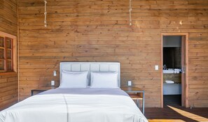 A wooden-paneled room with a bed, bedside tables, and a door leading to a bathroom. - Cabana vista Serra Catarinense VST023 (Anitápolis)