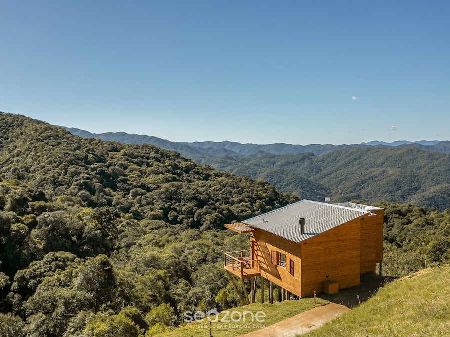 A wooden cabin with a balcony, surrounded by forested hills.