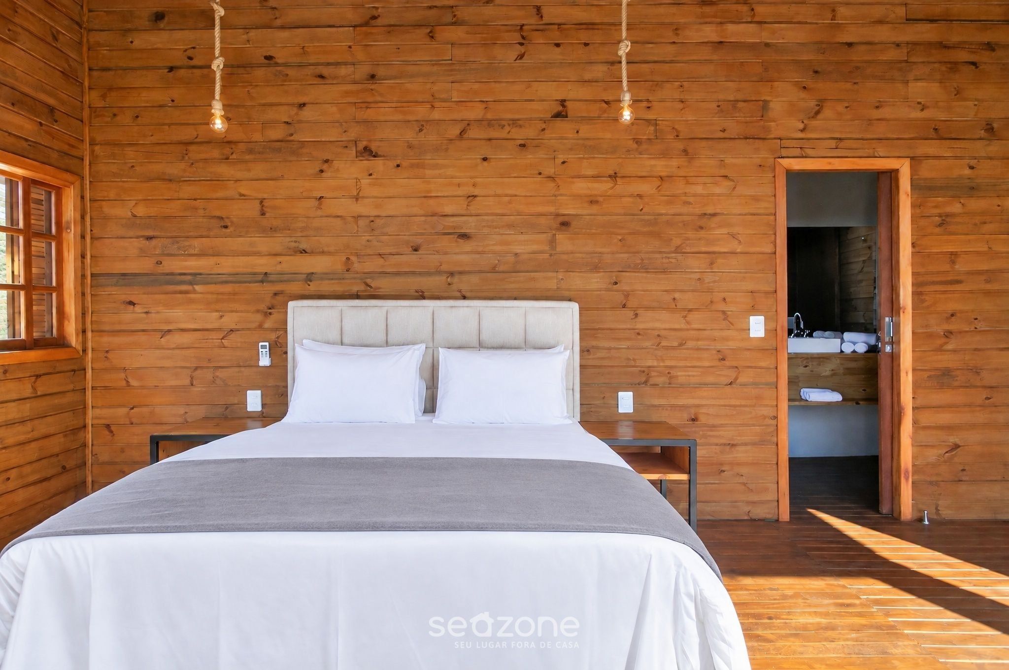 A wooden-paneled room with a bed, bedside tables, and a visible bathroom.