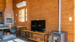 A cozy cabin interior with a brick fireplace, a TV, wooden furniture, and a small kitchen area. - Cabana vista Serra Catarinense VST023 (Anitápolis)