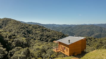 A wooden cabin with a balcony, surrounded by forested hills.