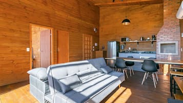 A cozy cabin interior with a sofa, dining table, chairs, and a kitchen area.