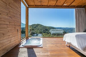 A wooden room with a large window, a hot tub, and a bed.
