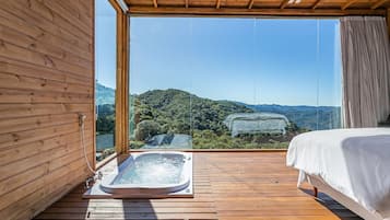 A wooden room with a large window, a hot tub, and a bed.