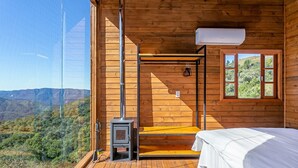A wooden cabin with a bed, a small stove, and a window overlooking a mountainous landscape. - Cabana vista Serra Catarinense VST023 (Anitápolis)