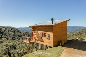 Una cabaña de madera con balcón, con montañas al fondo.
