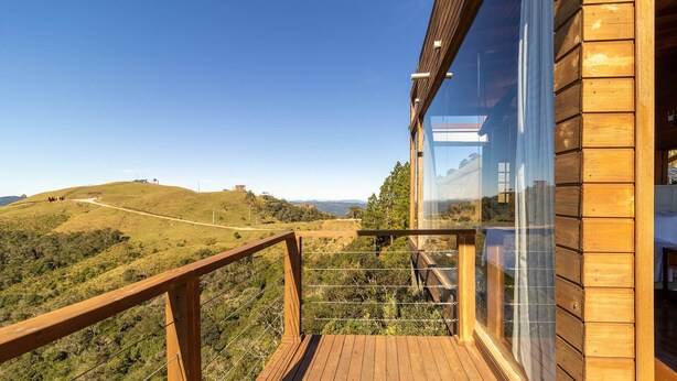 Una terraza de madera con barandilla de vidrio que da a un paisaje montañoso.
