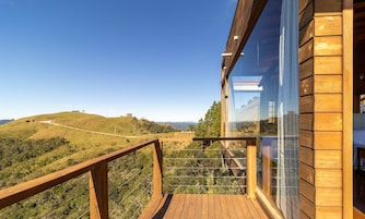 A wooden deck with a glass balustrade overlooking a hilly landscape.