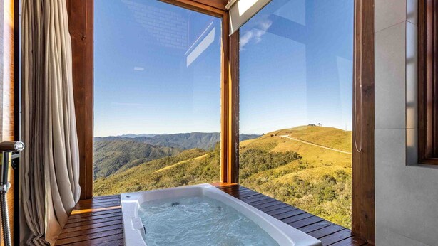 A hot tub on a wooden deck with a view of a hilly landscape. - Cabana espetacular região serrana VST008 (Anitápolis)