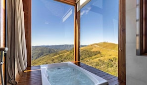 A hot tub on a wooden deck with a view of a hilly landscape.