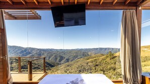 A bedroom with a large window overlooking a mountainous landscape. - Cabana espetacular região serrana VST008 (Anitápolis)
