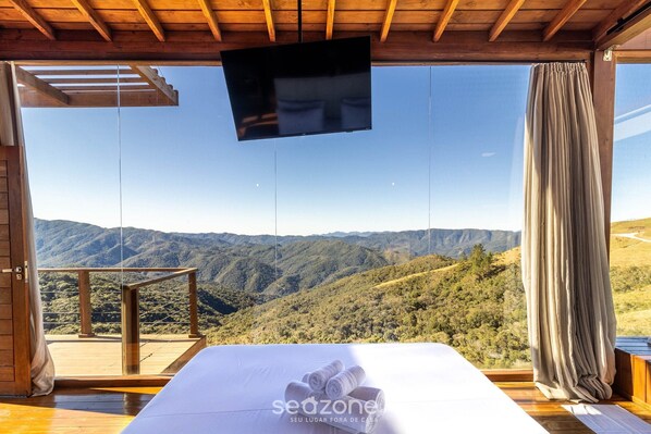 A bedroom with a large window overlooking a mountainous landscape. - Cabana espetacular região serrana VST008 (Anitápolis)