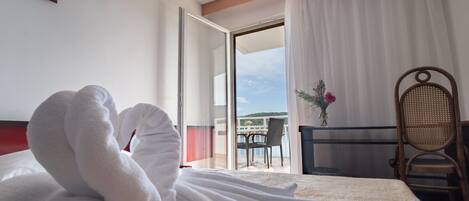 A hotel room with a bed, a chair, a table, and a view of the sea through a glass door.