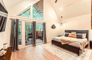 A bedroom with a large bed, a view of the outdoors through a sliding door, and a ceiling fan.