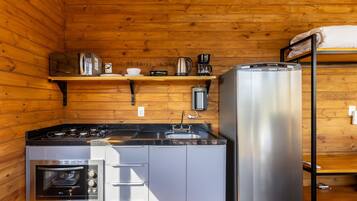 A compact kitchen with a stove, oven, refrigerator, and a coffee maker on a shelf.