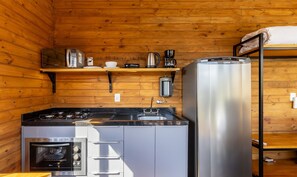 Cocina compacta con estufa, horno, refrigerador y cafetera sobre una estantería.