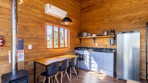 A compact kitchen with a stove, refrigerator, and a window overlooking greenery. - Chalé c\Jacuzzi prox. de Florianópolis VST024 (Anitapolis)