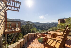 A wooden deck with a table and chairs, overlooking a mountainous landscape.