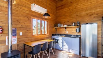 Une cuisine compacte équipée d’une cuisinière, d’un réfrigérateur et d’une fenêtre donnant sur un espace verdoyant.