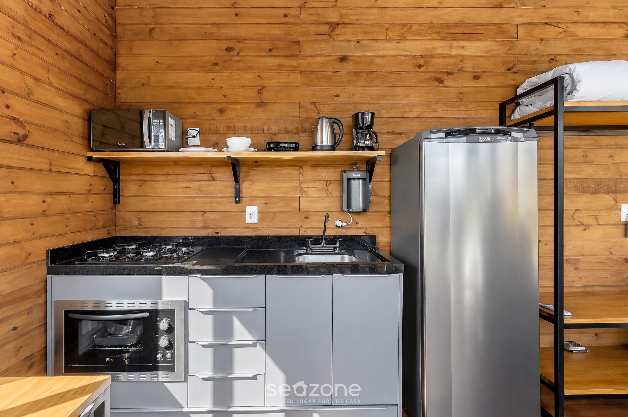 Een kleine keuken met een fornuis, oven en koelkast, voorzien van diverse apparaten en keukengerei.