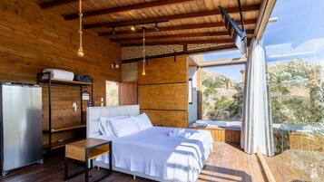 A modern bedroom with a bed, a small table, a built-in heater, and a view of the outdoors.