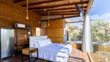 Une chambre à coucher moderne avec un lit, une petite table, une lampe suspendue et une vue sur l’extérieur.