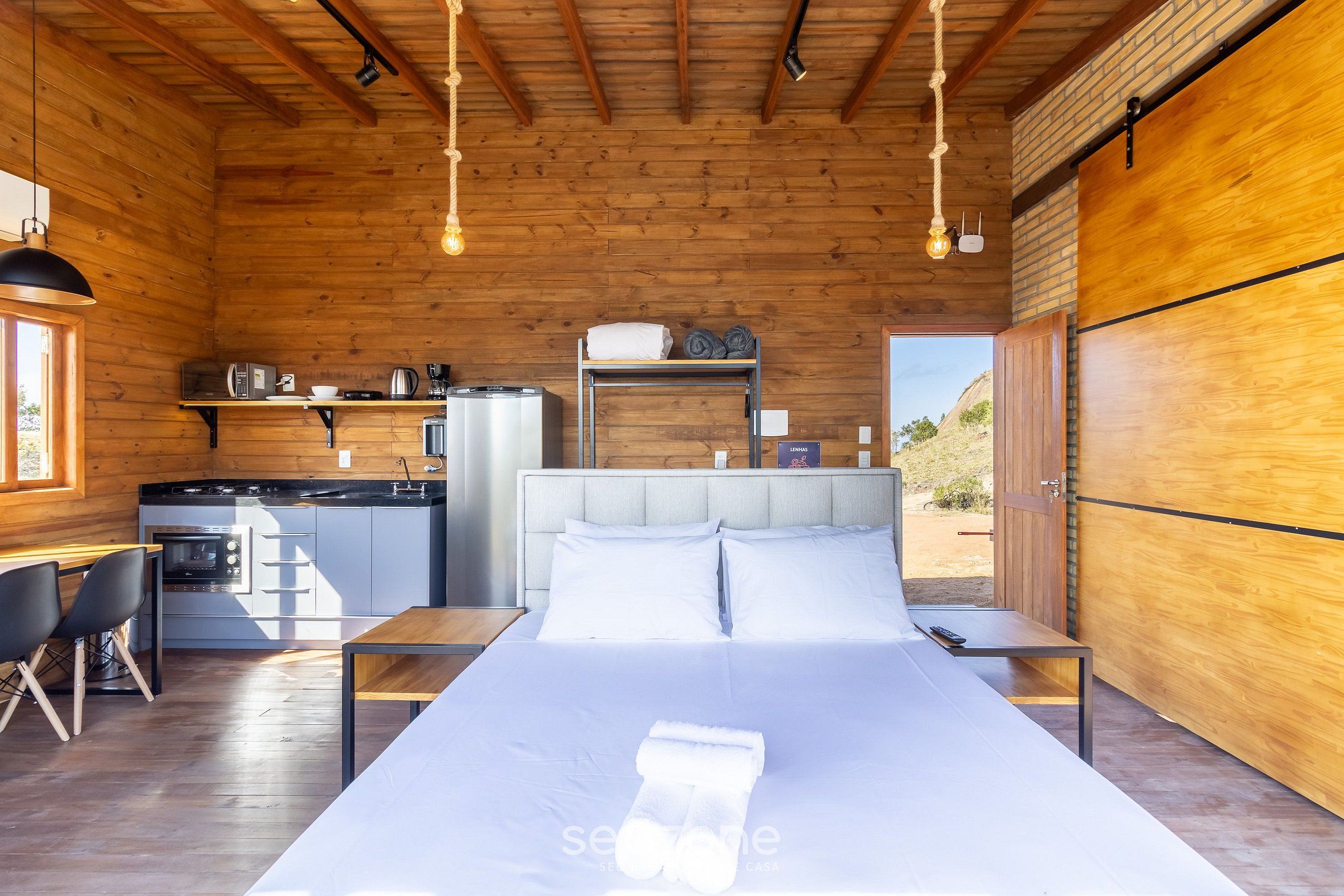 A wooden cabin with a bed, a kitchenette, and a dining area.