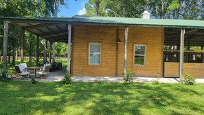 A wooden cabin with a covered porch, a seating area with chairs and a table, and a small garden.