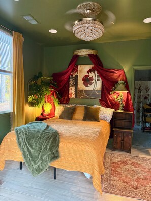 A bedroom with a bed, a chandelier, a red canopy, and a large window with curtains.